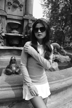 Elegant black and white portrait of a woman in fashion by a fountain.
