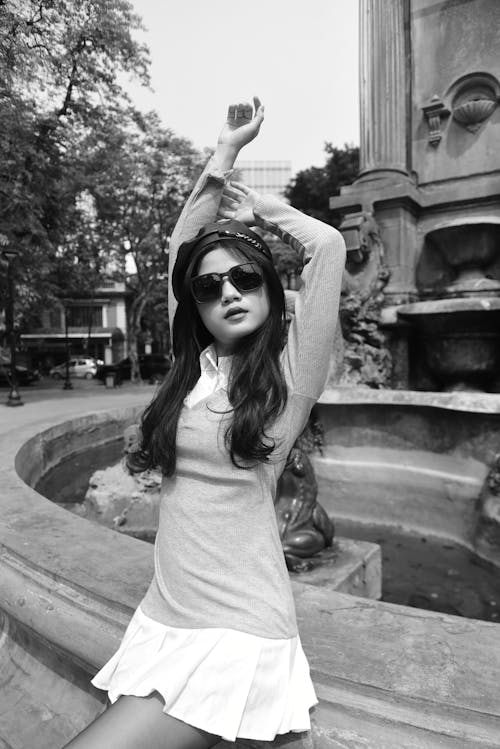 A woman in a dress and sunglasses posing near a fountain