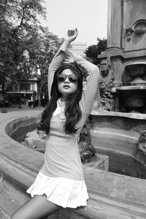 A woman in a dress and sunglasses posing near a fountain