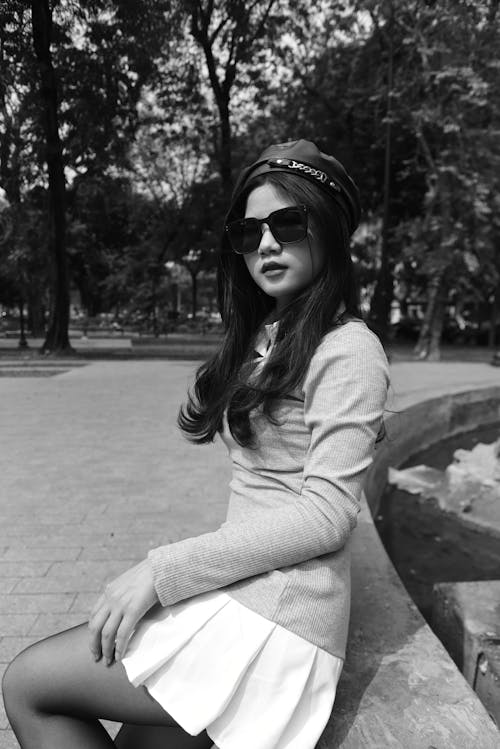 A woman in a skirt and sunglasses sitting on a bench