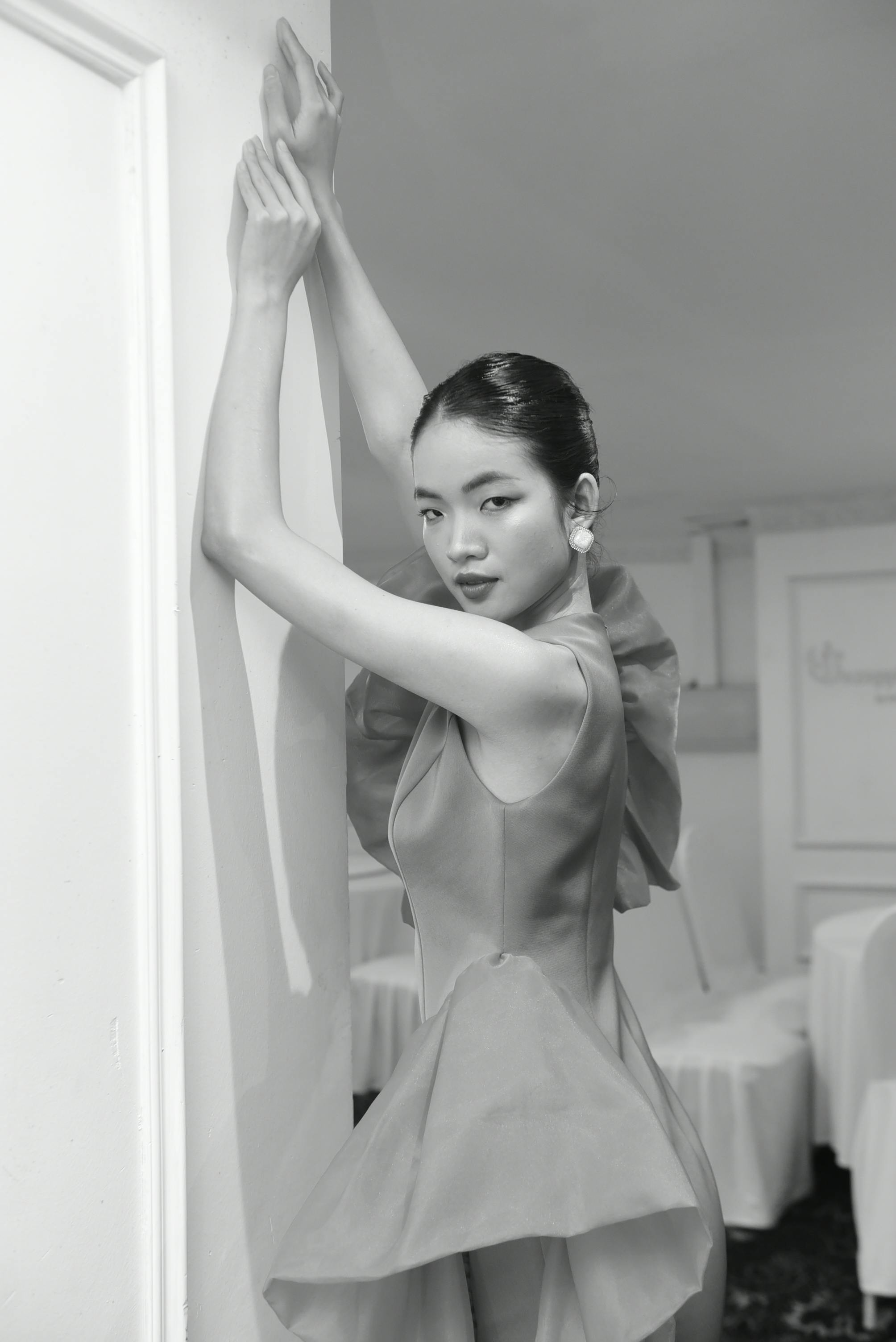 Sophisticated Asian woman posing in a stylish dress against a wall in monochrome.