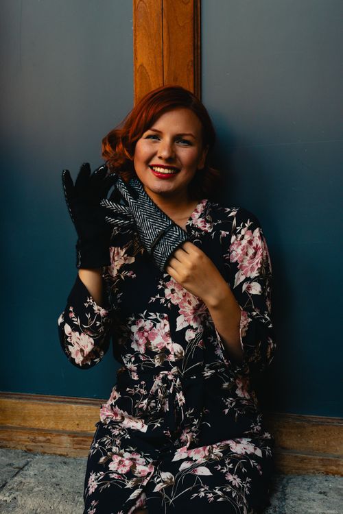 Free Redheaded woman in floral dress posing with black gloves, smiling warmly. Stock Photo