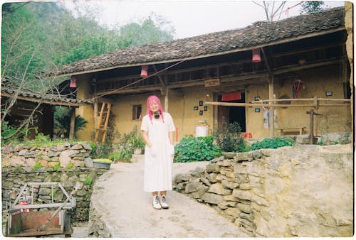 A woman in a white dress standing in front of a house