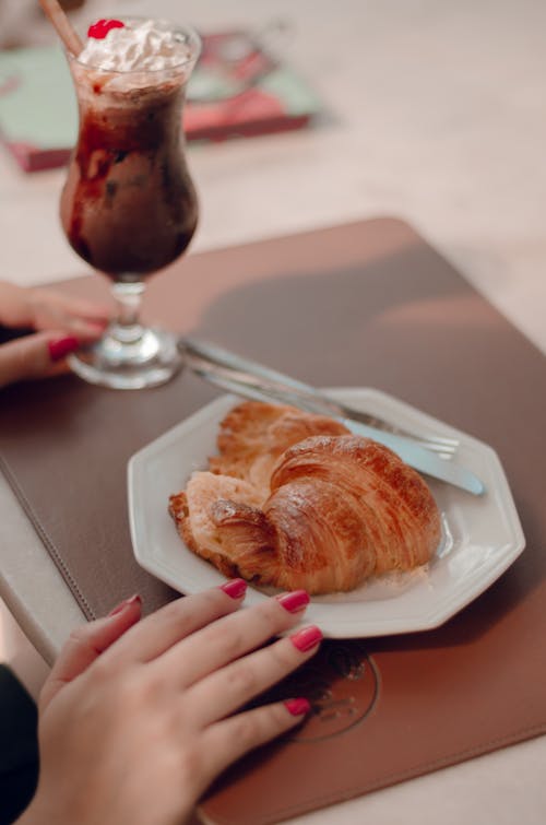 A woman's hand holding a croissant and a drink