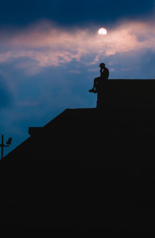 Free A serene silhouette of a person sitting atop a rooftop against a vibrant sunset in Coatzacoalcos, Mexico. Stock Photo