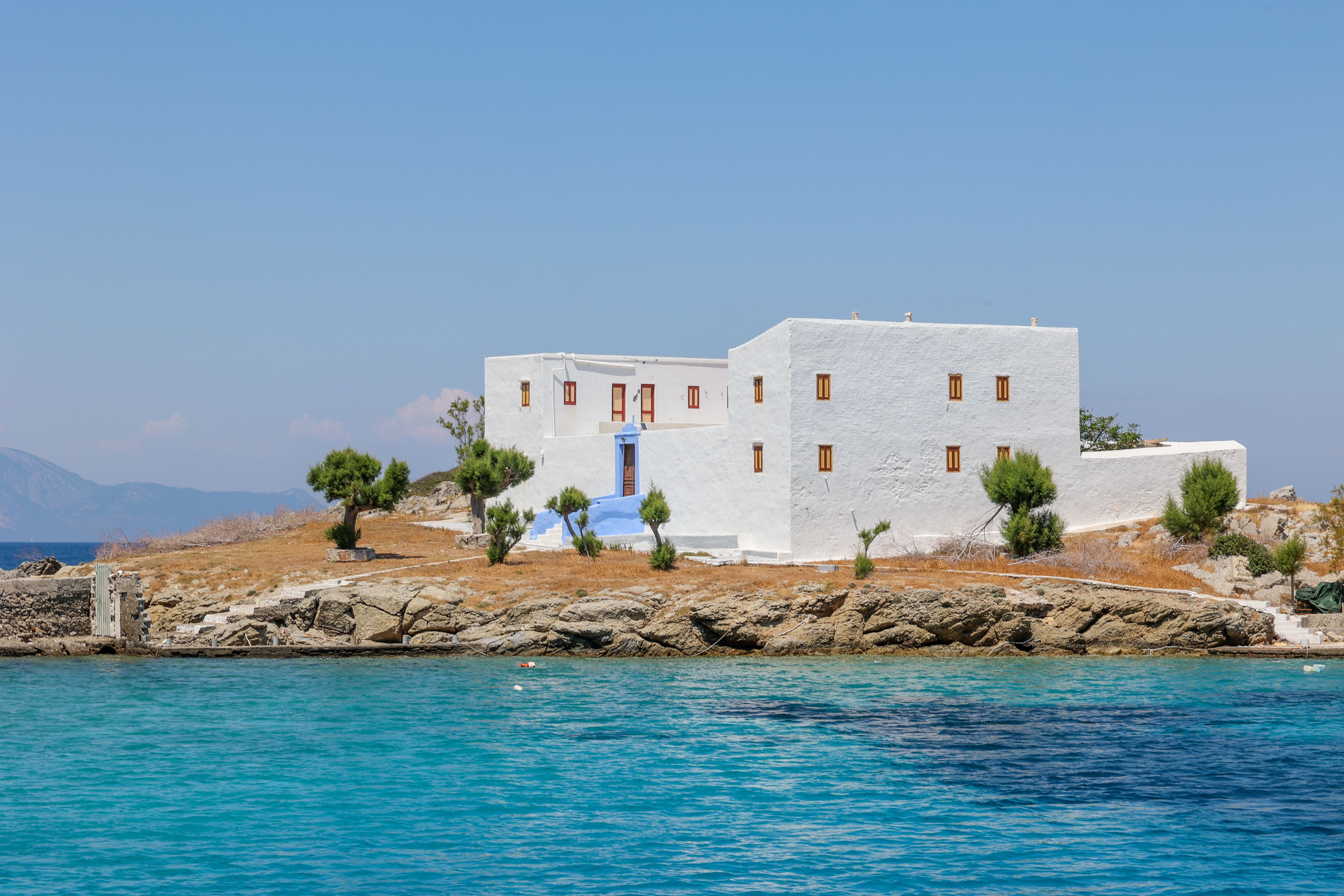 Scenic view of a white building on a small Greek islet surrounded by crystal blue water.