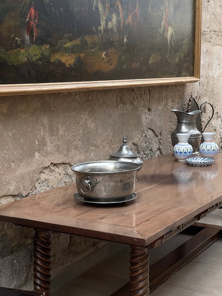 Silver Antique Kitchenware On A Wooden Table By A Piece Of Art Handing On The Wall