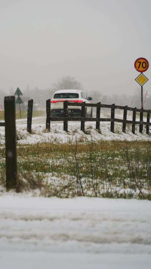 A car drives down a snowy road near a fence