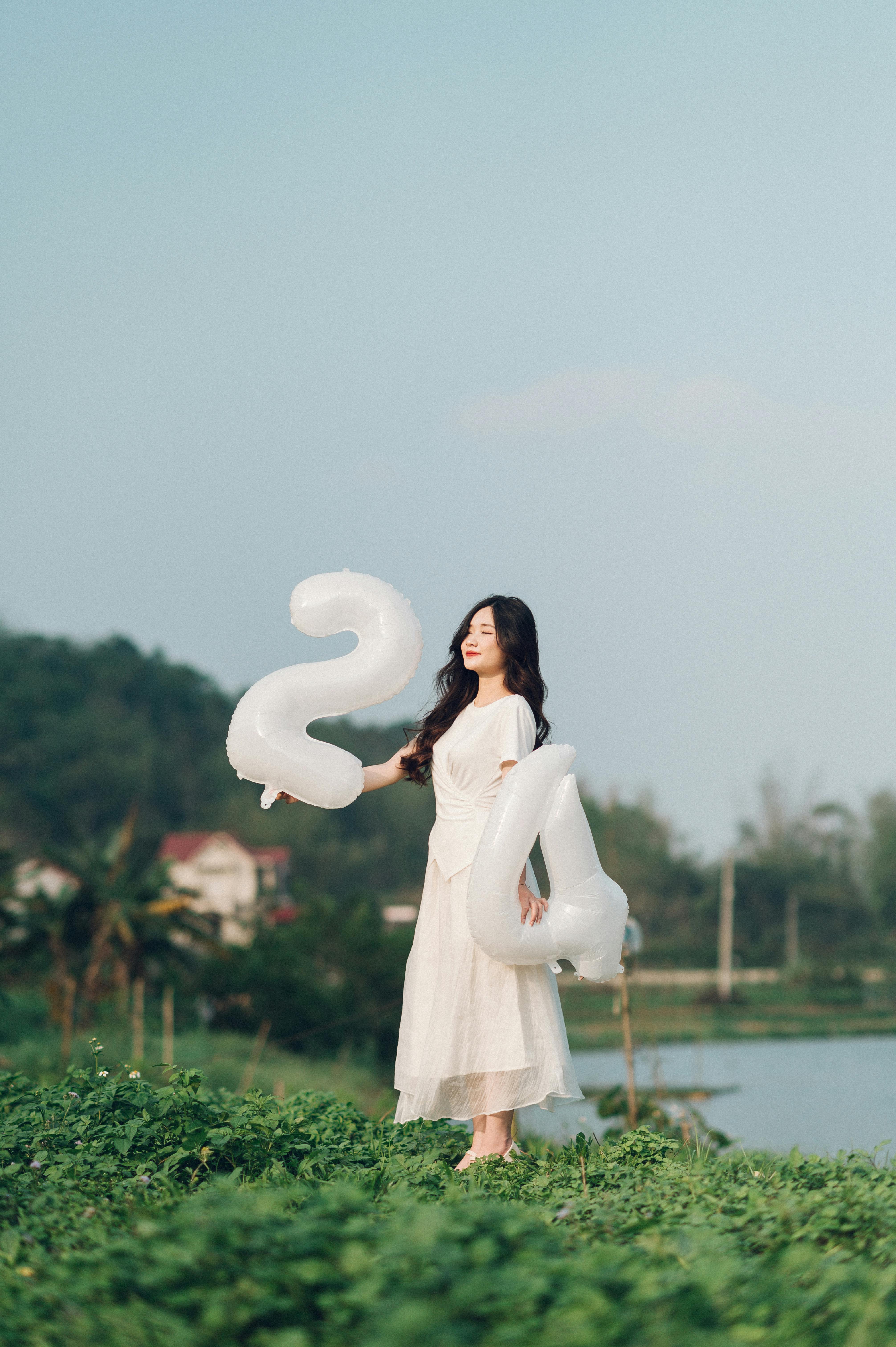 woman in white dress standing with birthday balloons