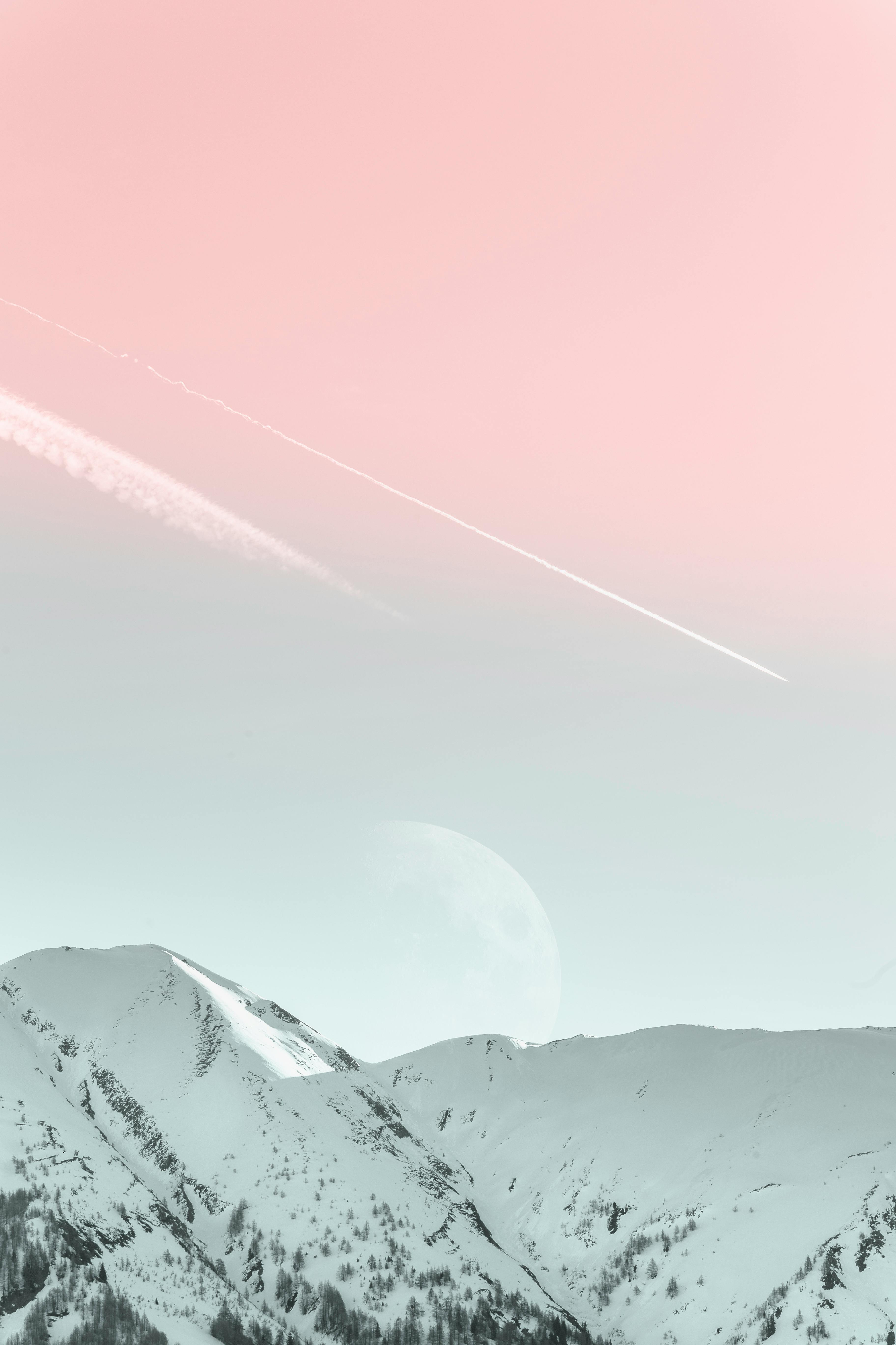 A tranquil winter landscape showcasing snowy mountains with a pastel-colored sky and visible moon.