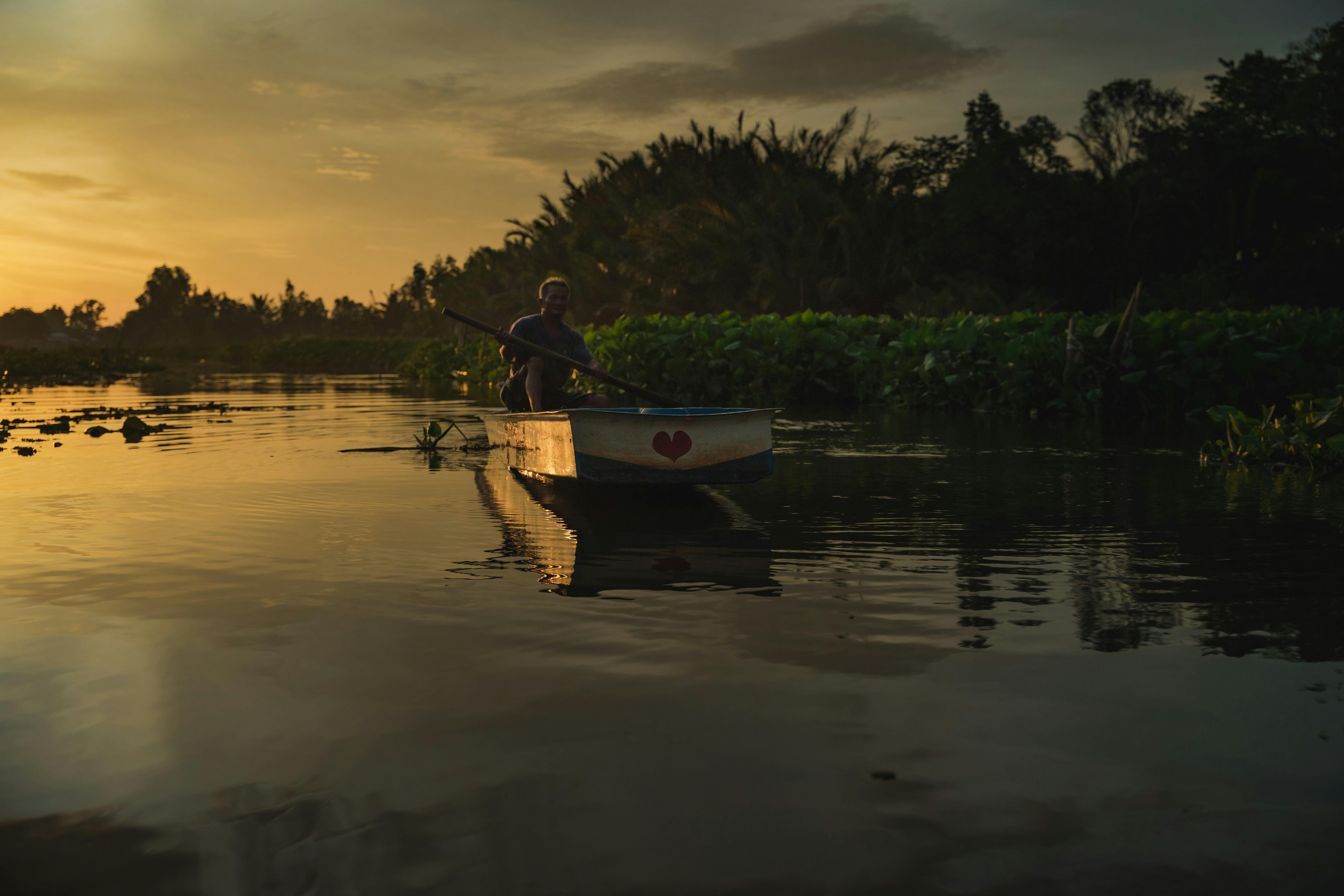 A serene scene of a boatman navigating a Vietnamese waterway during sunset in Hậu Giang.