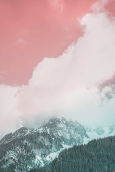 A scenic view of a snow-capped mountain beneath a pink-hued cloudy sky.