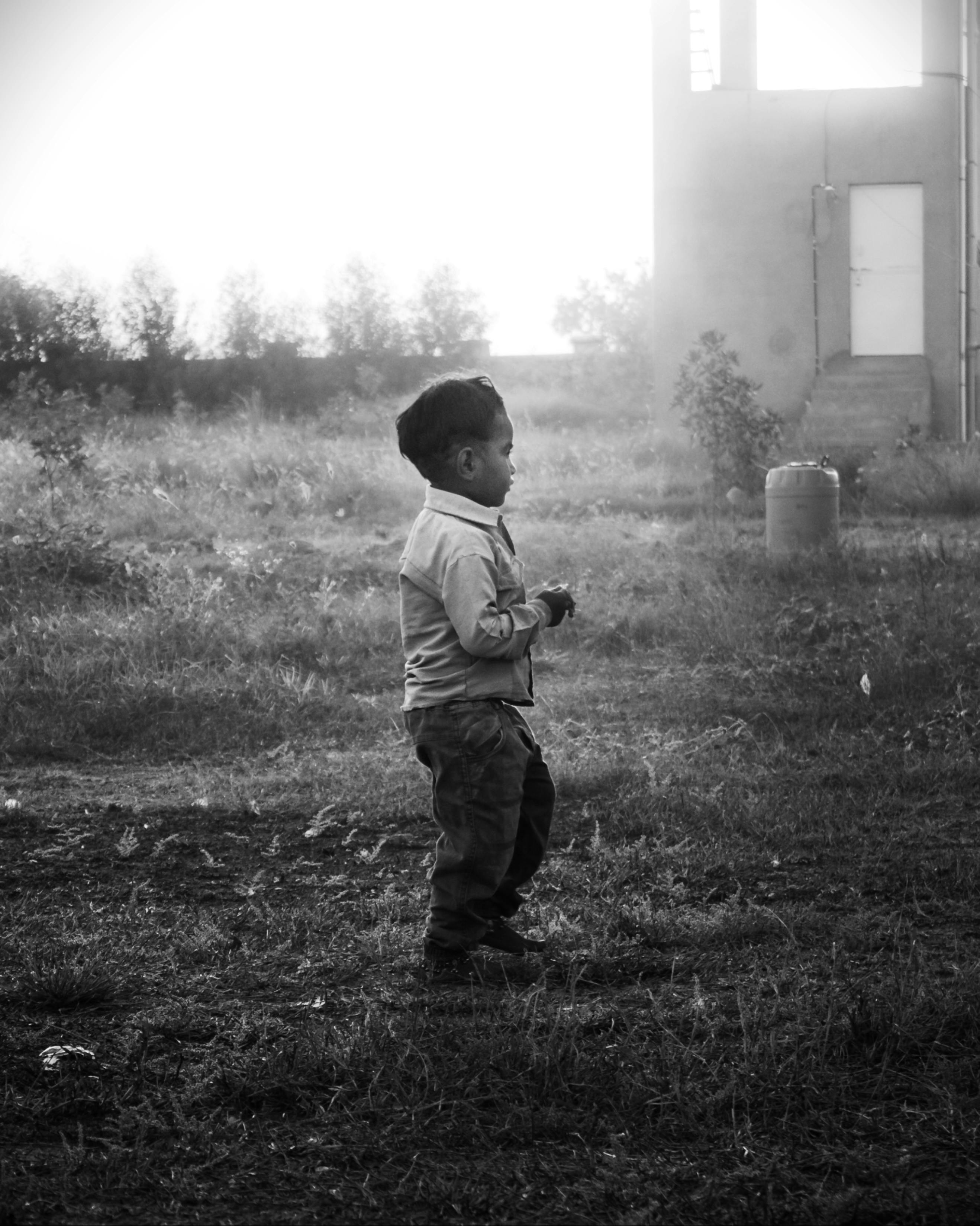 A young boy enjoys a serene moment in a sunlit field outside a rural building in India. | Indian Village Development