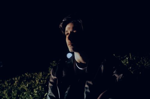 Free A man poses in a dimly lit garden at night, creating a mysterious atmosphere. Stock Photo