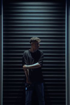 A man holding a camera stands against a moody urban backdrop at night.