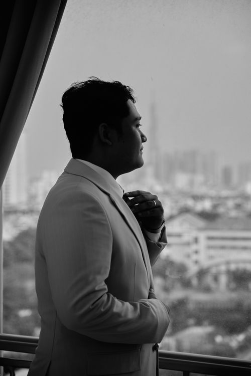 Free A man in a suit gazes thoughtfully out of a window with a cityscape in view. Stock Photo