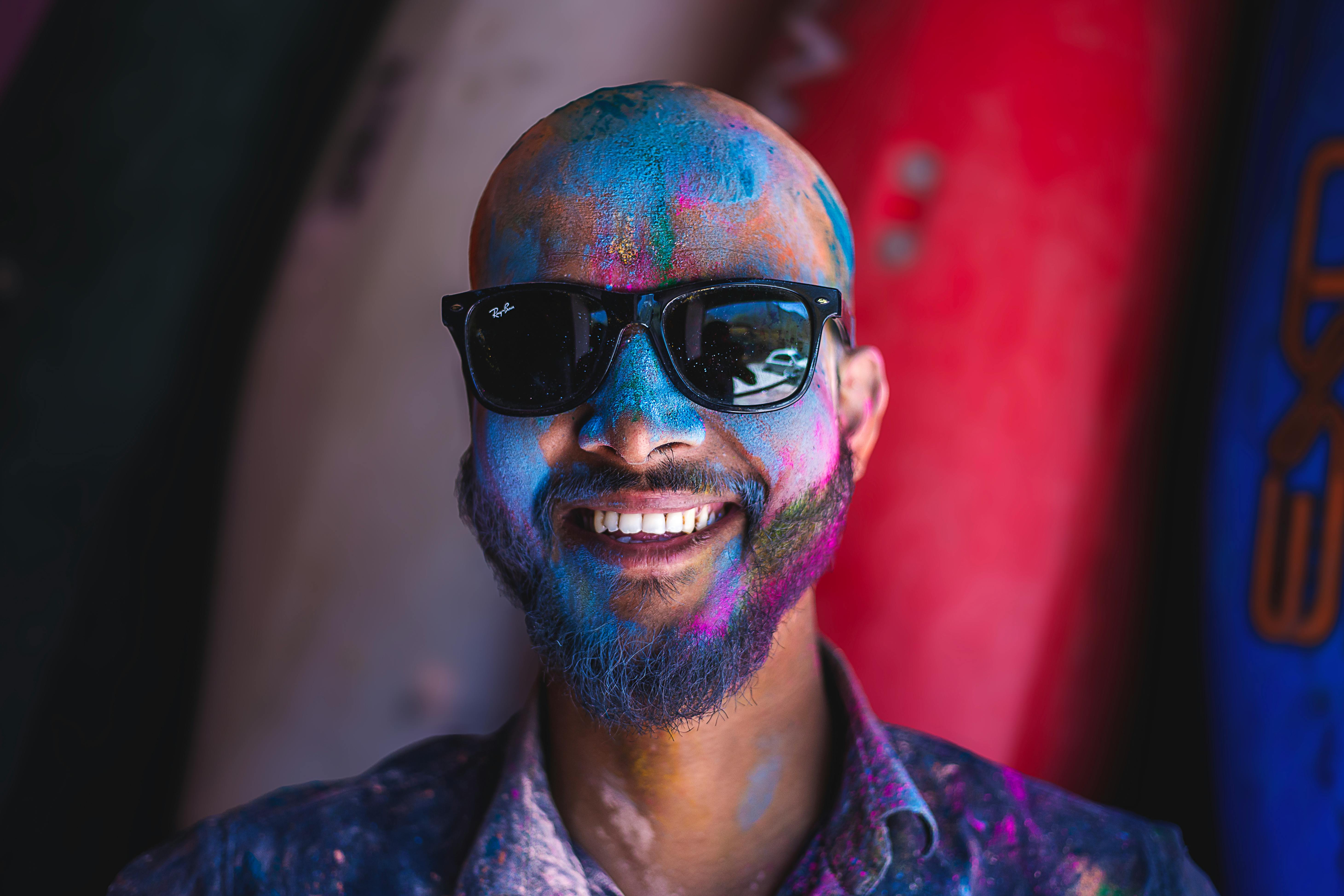 blue powder on face of smiling bald man in sunglasses