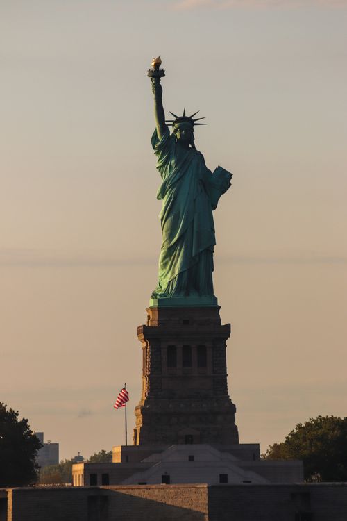 Free Iconic Statue of Liberty against a clear sky at sunset, a symbol of freedom in New York City. Stock Photo