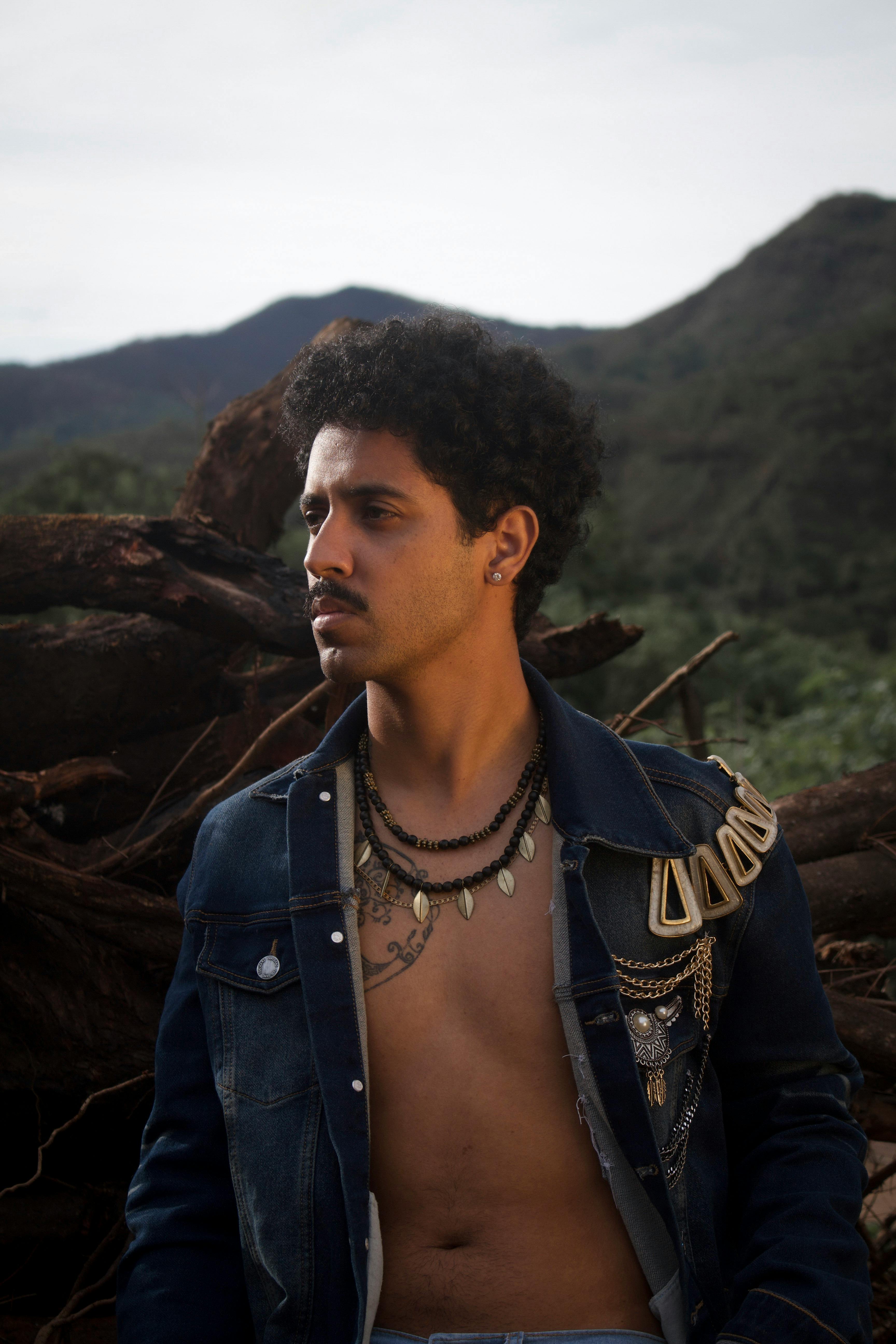 一位时尚男士身着牛仔夹克，以山景为背景在户外摆出姿势