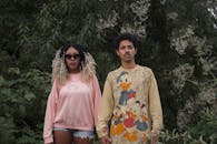 一对时尚情侣自信地站在郁郁葱葱的绿化中，展示着休闲服饰与独特风格