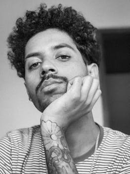 一幅黑白肖像中，一个男人纹着身，卷发，手托下巴，若有所思