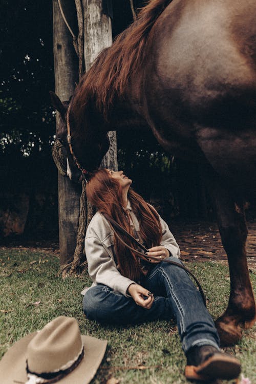 A Woman Sitting next to a Brown Horse