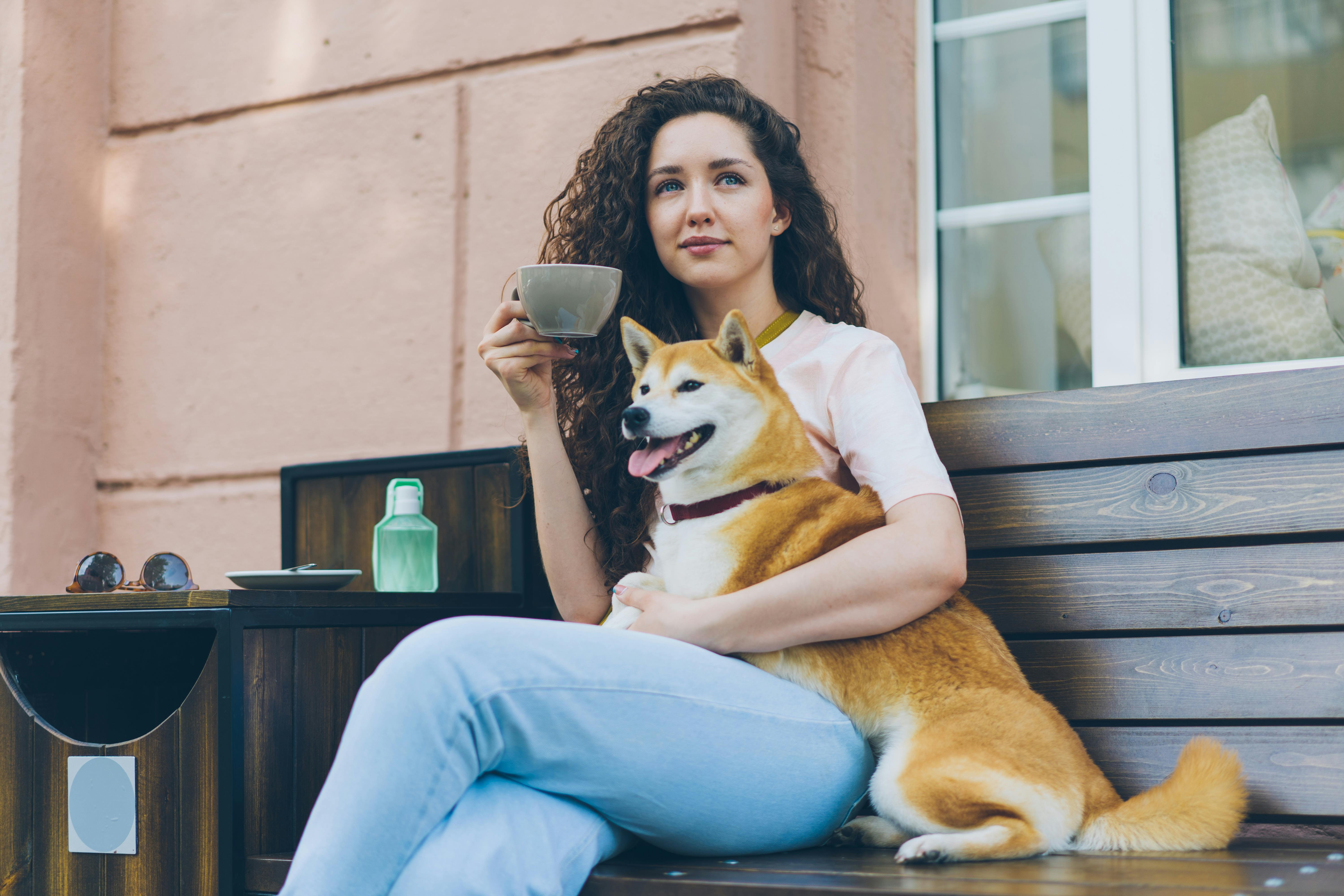 Woman Sitting with Cup and Hugging Shiba Inu Dog on Bench