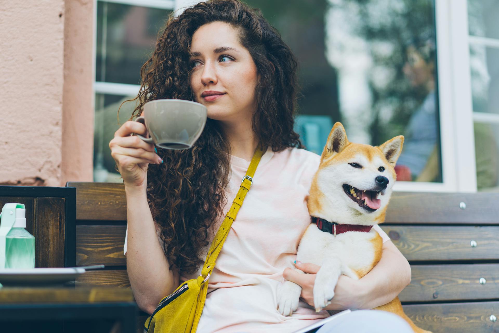 En ung kvinna sitter på en bänk med en kopp kaffe och sin shiba-inu-hund