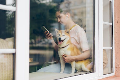 A woman sitting on the window sill with her dog