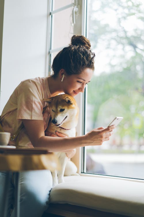 A woman holding a dog while looking at her phone