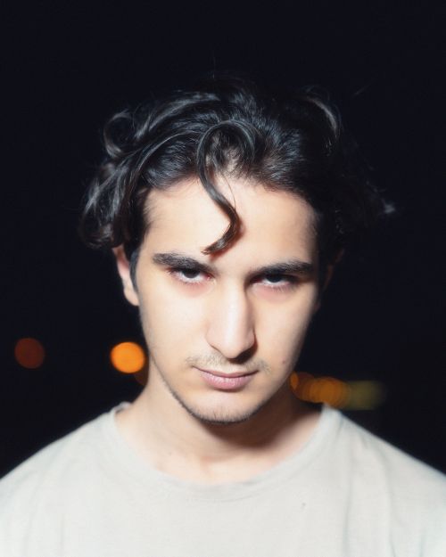 Free A portrait of a young man with dark hair posing outdoors at night, featuring dramatic lighting. Stock Photo