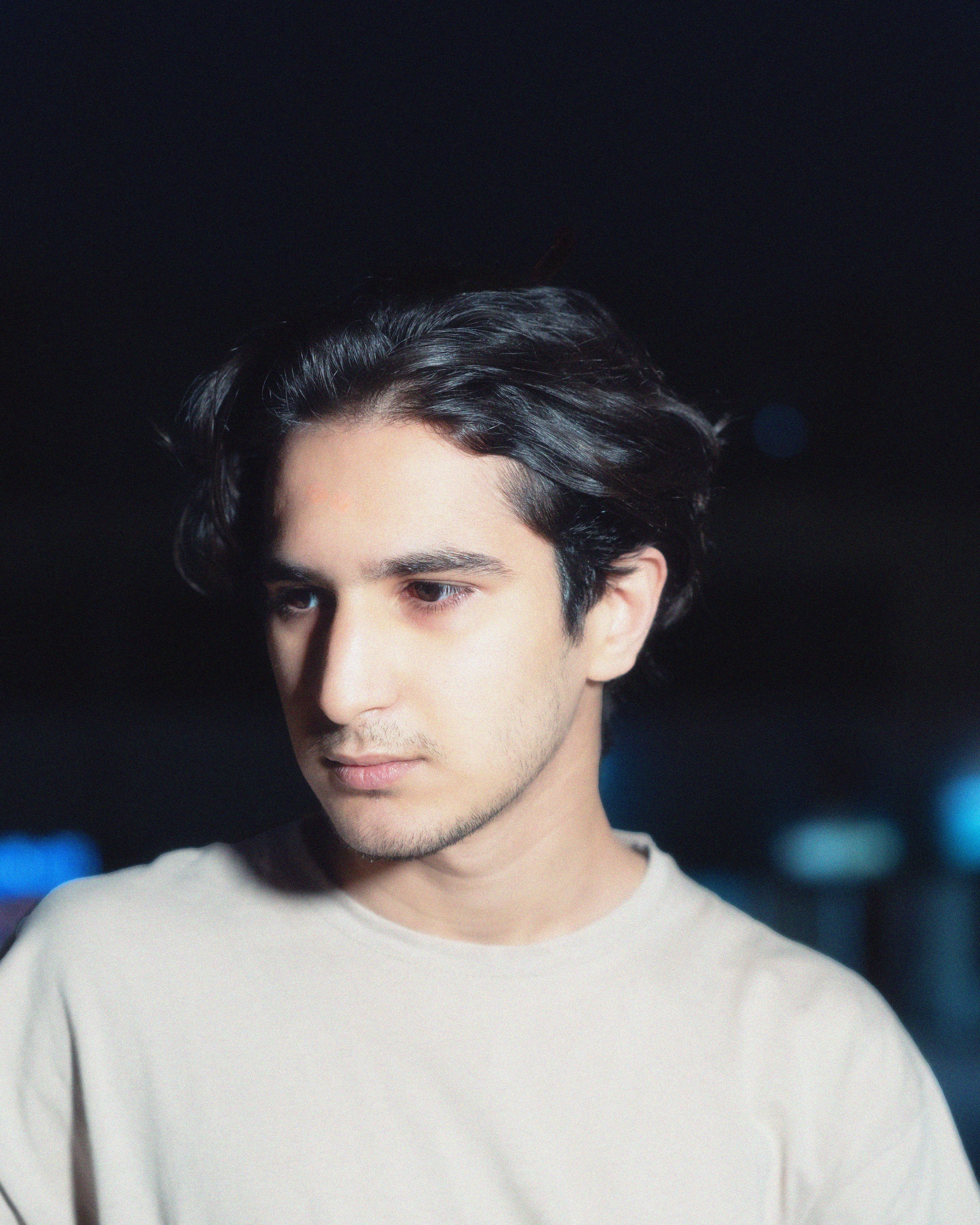 Portrait of a young man with dark hair at night, wearing a casual t-shirt. Deep expression and contemplative mood.