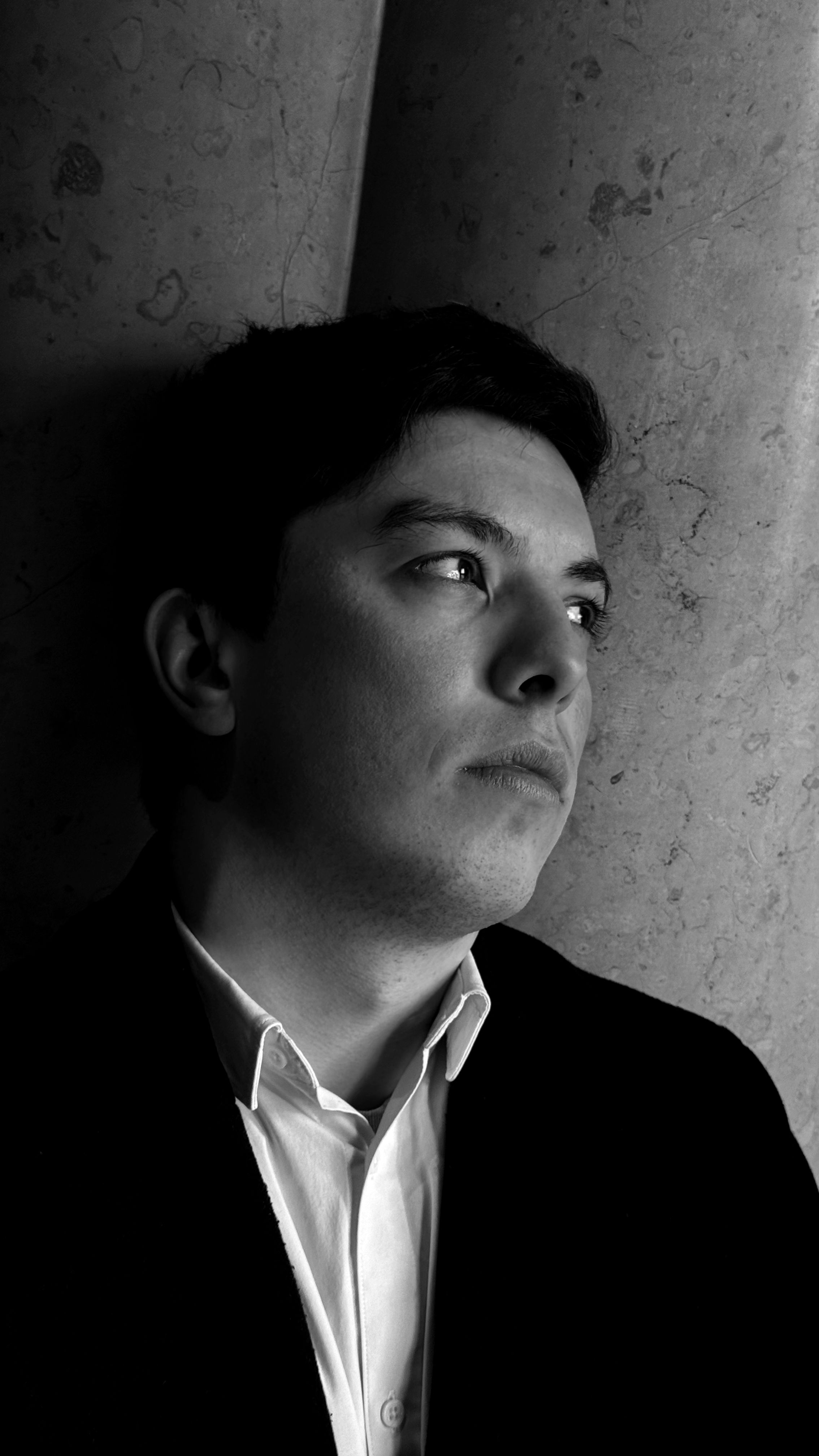 A black and white portrait capturing a pensive young man in a suit, looking away with a serious expression.