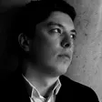 Black-and-white portrait of a noble young man in a dark blazer gazing away into the distance against a stone wall