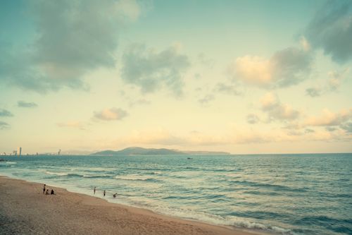 Free Serene beach scene capturing gentle waves, distant mountains, and a vibrant coastal skyline under a warm sky. Stock Photo
