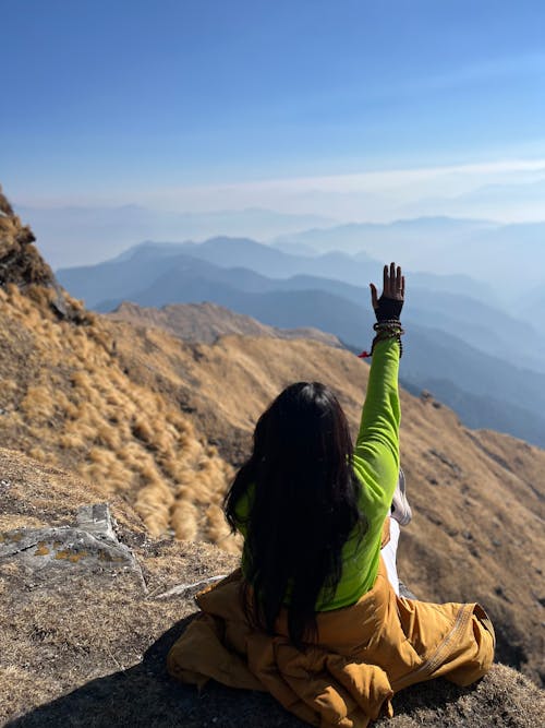 A woman sitting on top of a mountain with her hands up