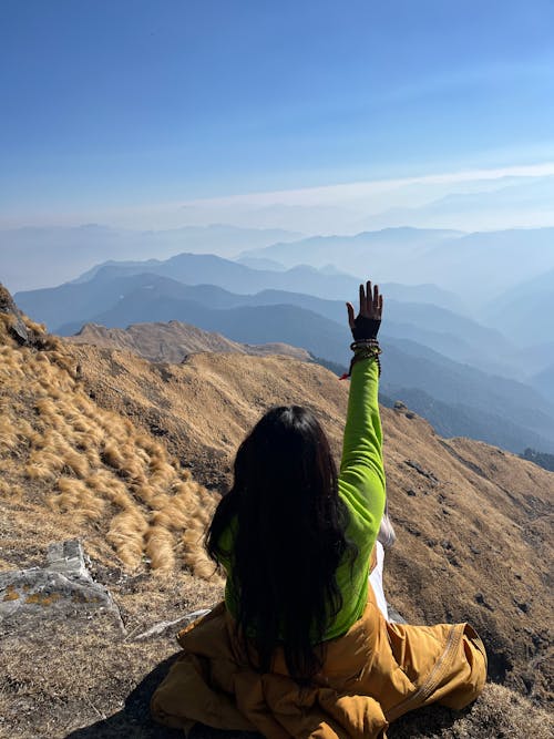 A woman sitting on top of a mountain with her hands up