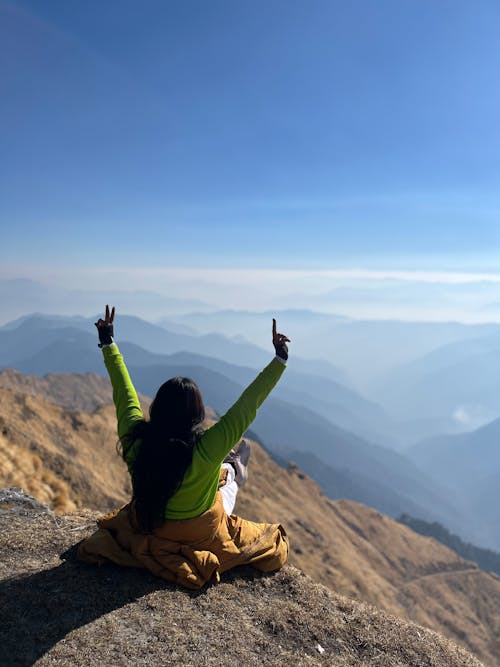 A woman sitting on top of a mountain with her hands up