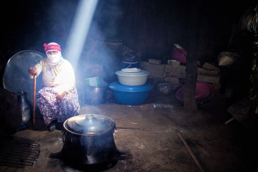 A woman cooks in a rustic home with sunbeam illumination, evoking simplicity and tradition.
