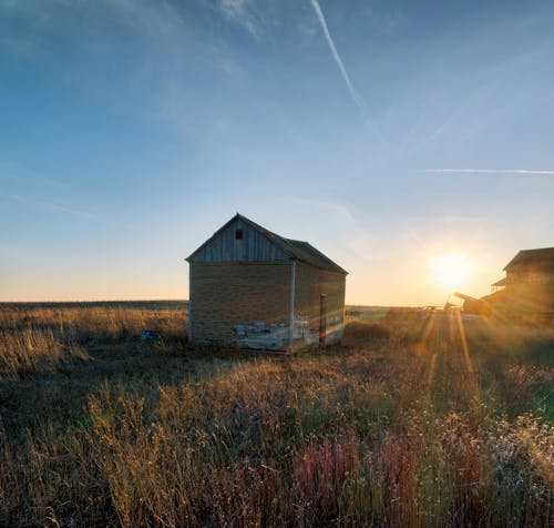 A barn sits in the middle of a field at sunset