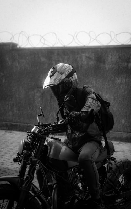 Free Black and white portrait of a motorcyclist sitting with helmet in an urban environment. Stock Photo