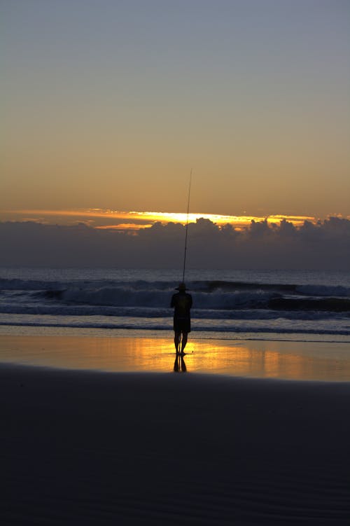 A man standing on the beach with a fishing pole