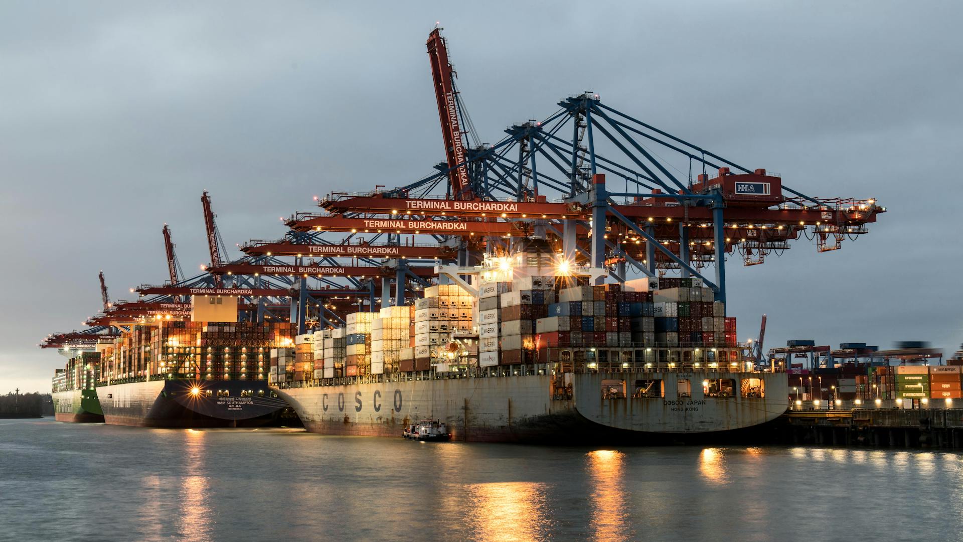 Container ships docked at Hamburg's Burchardkai Terminal during twilight, showcasing bustling maritime activity.