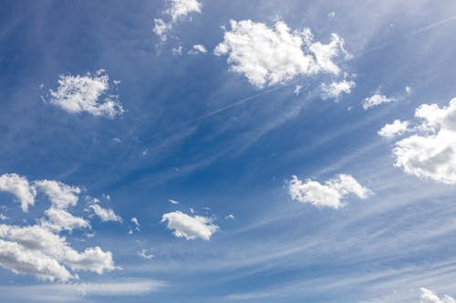 A blue sky with white clouds and a plane flying