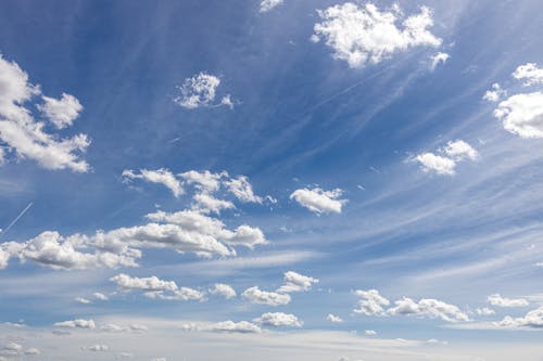 A blue sky with white clouds and a plane flying