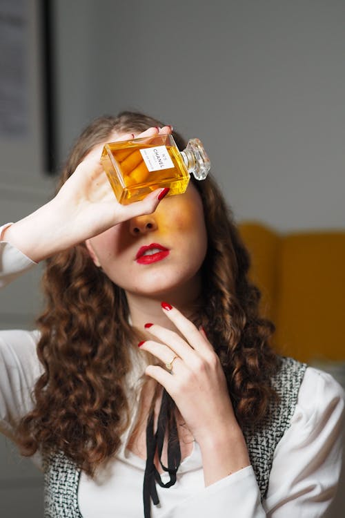 A woman holding a bottle of perfume in front of her face