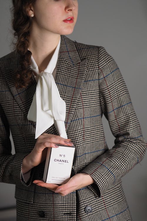 A woman in a suit holding a bottle of perfume