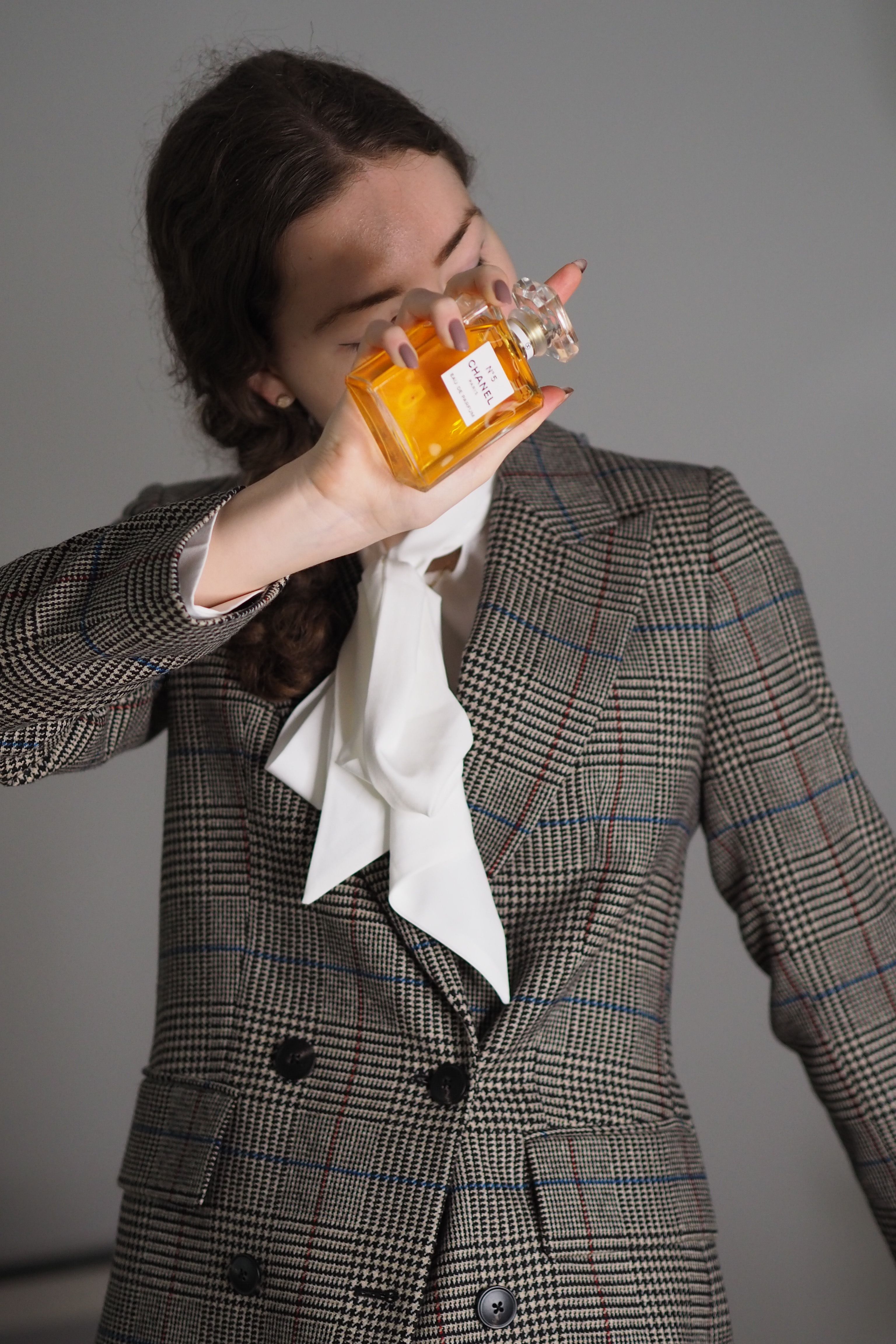 Mulher elegan te com um blazer xadrez segurando um frasco de perfume dentro de casa em Paris.