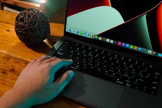 A hand interacting with a laptop on a wooden desk, next to a decorative ball.