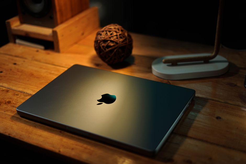 A sleek laptop on a wooden desk with warm ambient lighting, creating a cozy workspace atmosphere.